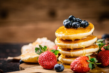 A pile of pancakes with fresh berries and honey on the table. 