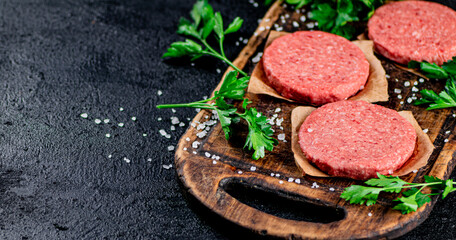 Raw burger on a wooden cutting board with parsley. 