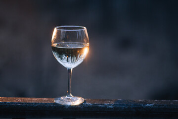 glass of white wine outside at sunset with the blurry background and the reflection of  the forest