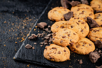 Cookies with pieces of milk chocolate on a stone board. 
