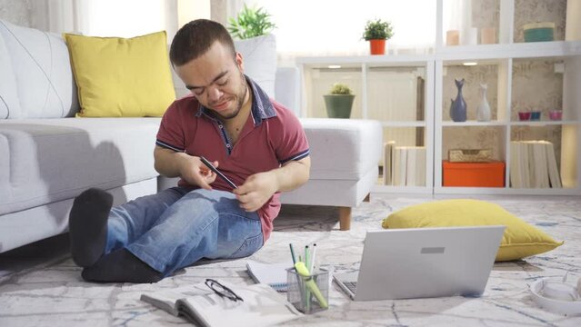 Young male student with dwarfism studying at home and enjoying himself.
College student young man with dwarfism studying at home, disabled young student using laptop.
