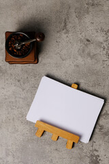 High angle of blank white paper on wooden display frame and coffee grinder with coffee beans on abstract background. Space for text.