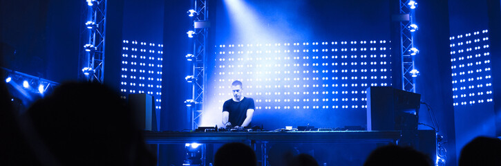 Dj playing techno music on the concert stage on a summer night