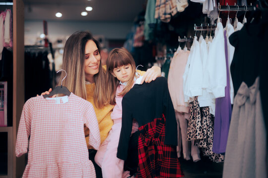Mother and Toddler Daughter Choosing a Dress in Fashion Store. cheerful mom and girl comparing two garments deciding what to purchase
