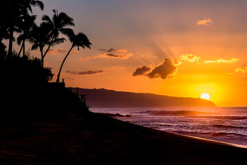 Sun setting behind the mountain over waves and palm trees on Sunset Beach, Hawaii - obrazy, fototapety, plakaty