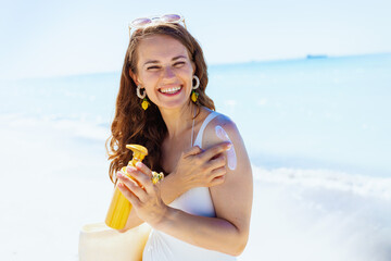 Portrait of smiling stylish woman at beach applying spf