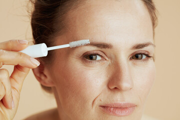 Closeup on young female with brow brush on beige background