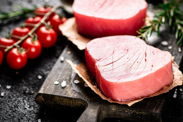Raw tuna on a cutting board with tomatoes and rosemary. 