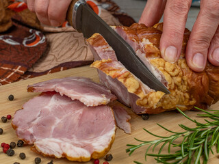 A piece of juicy and tasty bacon is cut with a kitchen knife into appetizing pieces. Close-up of female hands cutting a piece of ham into slices. The concept of cooking meat