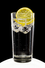 Glass of sparkling mineral water with ice and lemon slice on black background