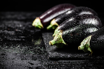 Fresh ripe eggplant with droplets of water on a stone board. 