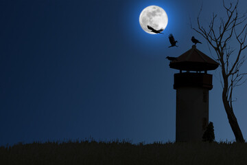 Fototapeta na wymiar Silhouette of a crow perching and flying on an old watchtower beside a dry tree on a blurred full moon night.