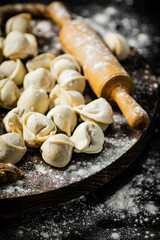 Raw homemade dumplings on tray with rolling pin. 