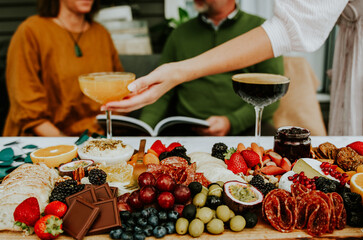 Lady reaching for a cocktail on a table with a grazing platter and a couple in the background talking.