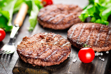 Burger grill on a cutting board with tomatoes and greens. 