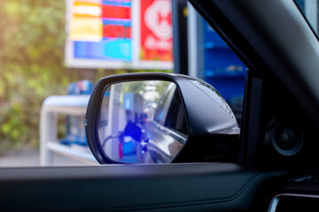 Selective focus to wing mirror with blurry fuel price display board and the officers are refueling in gas station.