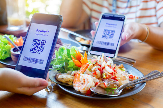 Selective focus to smartphone in hand to scan QR code on tag with blurry spicy Thai food. Customers in restaurant to accepted generate digital pay without money. Qr code payment concept.