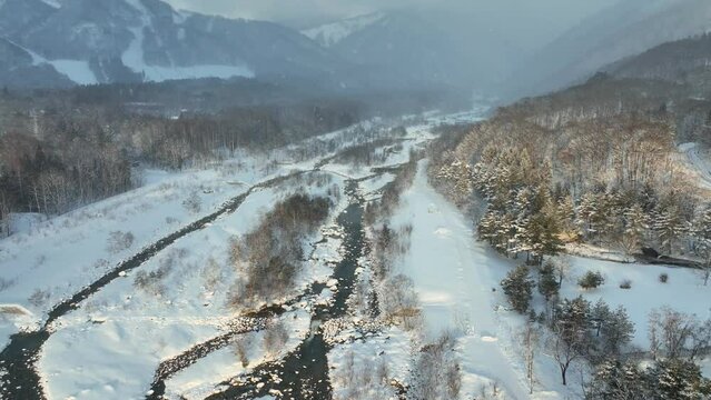 beautiful winter landscape of frozen river in the snowy mountains in Japan, Hakuba valley, frosty weather with below freezing temperatures, dreamy winter aerial view