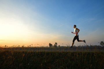 Side view of Asain man jogging on country road with sunrise background.