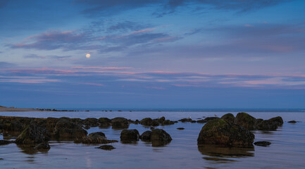 Obraz premium A seascape photo at sunrise with a full moon hanging in sky