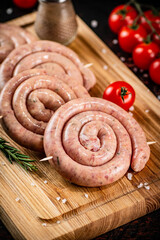 Raw sausages on a cutting board with a sprig of rosemary and tomatoes.