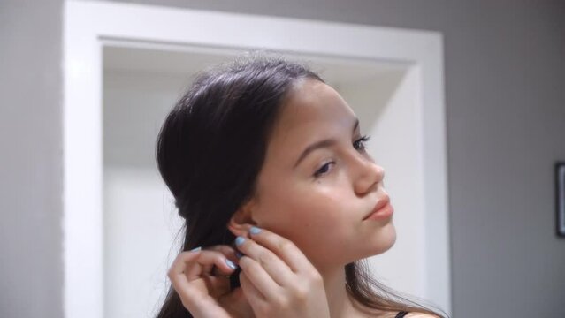 Beautiful hispanic girl putting earring looking in mirror in her bedroom at home