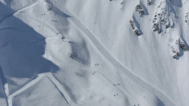 Aerial top view tourists people riding ski snowboard on track at mountain valley resort with ropeway cabins cinematic scenery. Drone shot extreme sport recreation adrenaline hobby leisure activity 4k