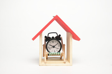 A picture of house miniature, alarm clock and folding beach chair on copyspace white background.