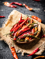 Pods of dried chili peppers in a wooden plate on a napkin. 