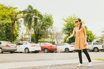 Beautiful blind asian woman crosses the road using cane to guide the walk slowly for safety while...