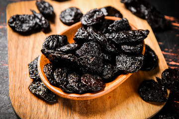 Prunes in a plate on a wooden cutting board. 