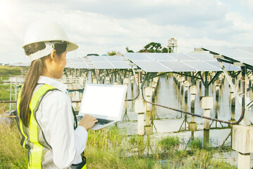Back view asian female electrical engineer in hard hat works in the field checking solar panel...