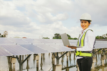 Professional asian female electrical engineer in hard hat works in the field checking solar panel installation site on suburban well typing results on tablet online system to connect to 