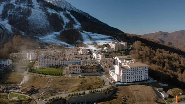 Ski resort luxury hotel not season infrastructure mountain snow peak sunny landscape aerial view. Drone shot building architecture exterior fall autumn spring forest tree cinematic alpine scenery 4k