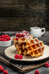 Belgian waffles with raspberries with sugar powder in a freeze motion of a cloud of powder midair, served with jug of milk. Delicious breakfast or snack. vertical image. top view. place for text