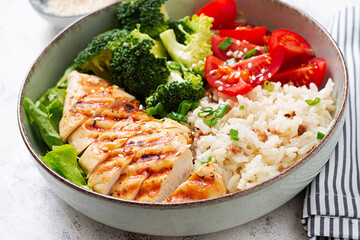 Delicious buddha bowl with grilled chicken, fresh vegetables and rice on a light background.
