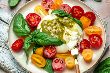 Salad with burrata cheese, cherry tomatoes and green pesto on a light background. Restaurant menu, dieting, cookbook recipe top view.