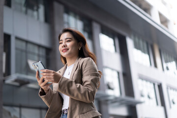 Fototapeta premium Portrait of young Asian business woman using digital tablet, professional manager holding digital tablet computer using software applications standing in front of modern business building