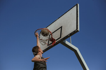 Low angle of man playing basketball and throwing ball in hoop on playground in summer 