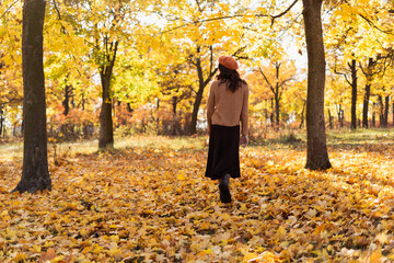 Back view of elegant young woman in orange beret in autumn. Cute girl walks in the park in golden autumn. Autumn walk.