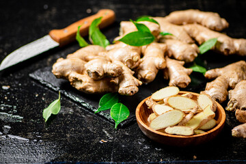 Pieces and whole ginger on a stone board with foliage. 