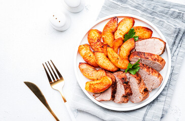 Baked pork tenderloin with quince or apple slices served on plate. White table background, top view