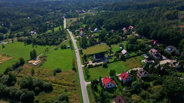 Mountain village and road with moving cars, aerial view. Beautiful mountain landscape with residential neighborhood and green fields. Countryside view