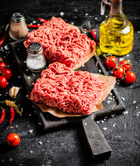 Raw minced meat on a cutting board with cherry tomatoes. 