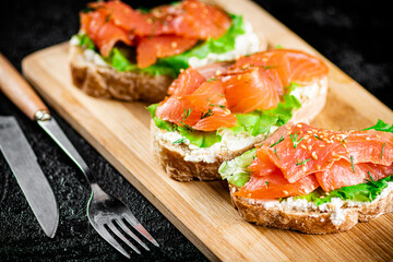 Sandwich with pieces of salmon on a cutting board. 