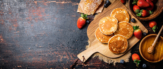 Obraz na płótnie Canvas Pancakes on a wooden cutting board with honey and berries.