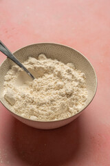 White flour in bowl over pink background, vertical image