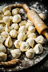 Raw dumplings on a wooden tray with a rolling pin and flour. 