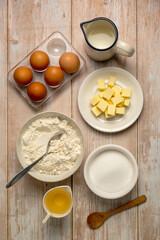 Baking ingredients, eggs, flour, butter, oil and milk. Top view, rustic wooden background.