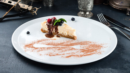 Piece of cheesecake with fresh raspberries and blueberries and chocolate and vanilla sauce.